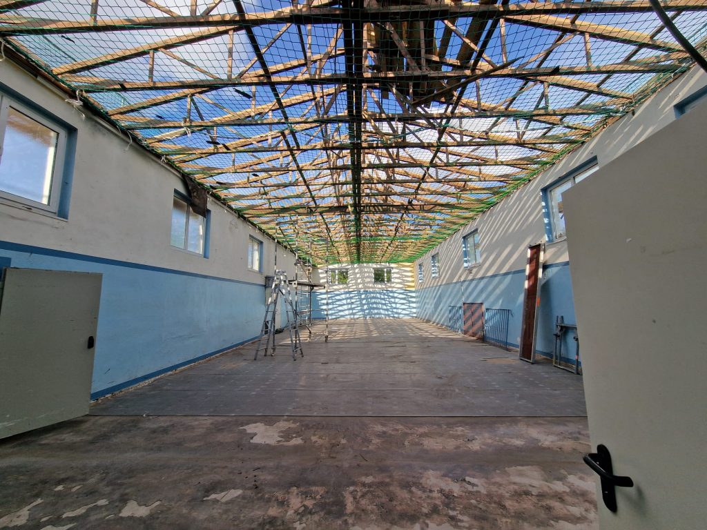 Blick in die entkernte Turnhalle mit offenem Dachstuhl und Netzsicherung
