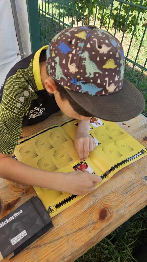 Kind klebt einen Sticker ins Sammelalbum beim Vereinsfest SV Concordia Schenkenberg