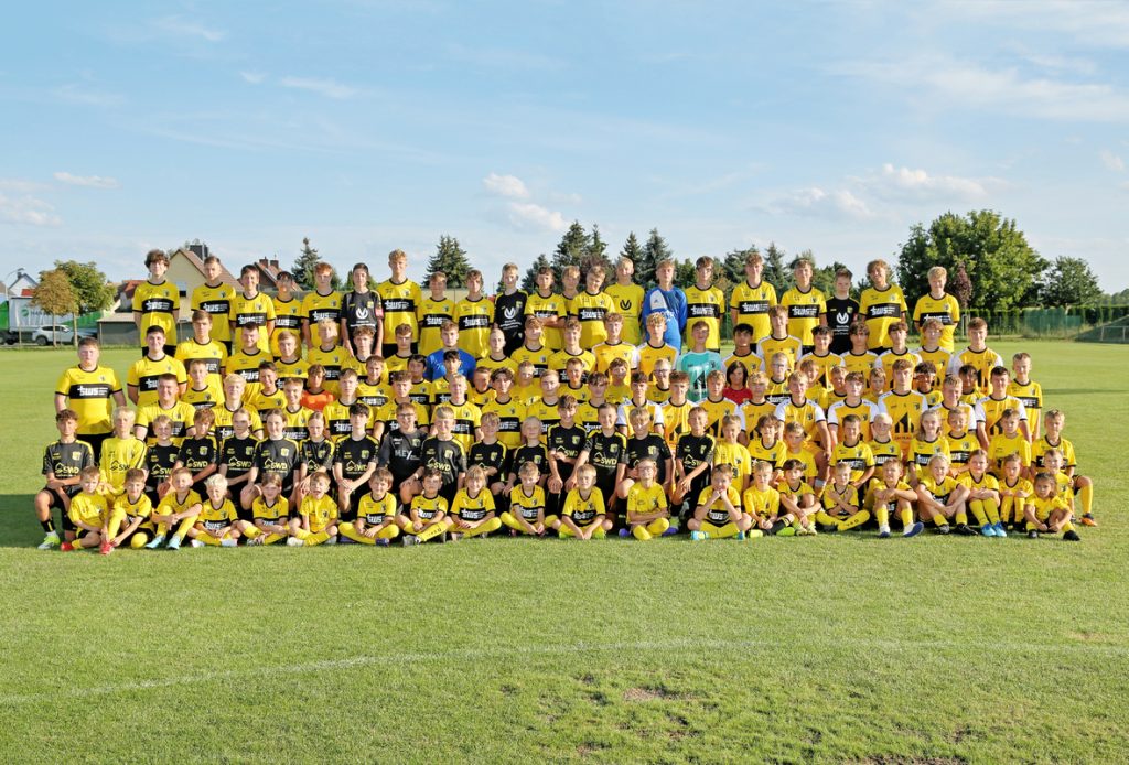 Vereinsfoto des SV Concordia Schenkenberg mit Kindern, Jugendlichen, Trainerinnen und Trainern in gelben Trikots auf dem Sportplatz